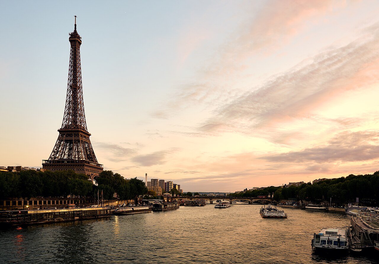 The Eiffel Tower over the Seine at sunset with river boats below