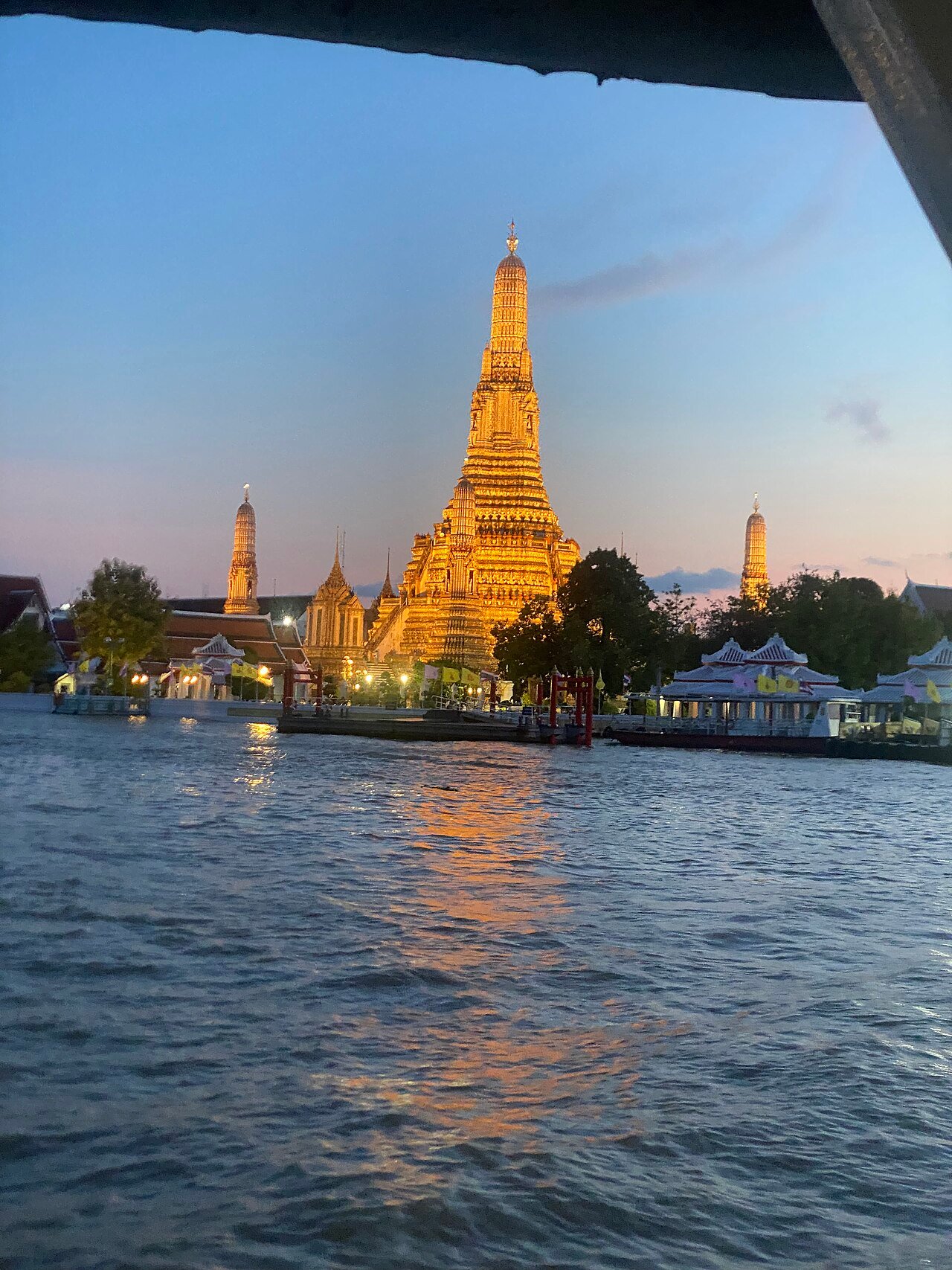 Wat Arun temple glowing golden at twilight seen from a boat on the Chao Phraya River